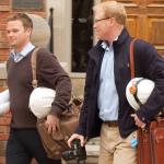 Two engineers with hardhats, plans, bags, and camera